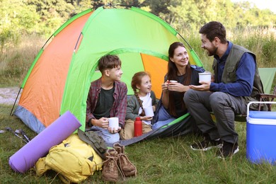 Photo of Happy family spending time together with camping tent, tourist equipment and mugs of hot drink outdoors