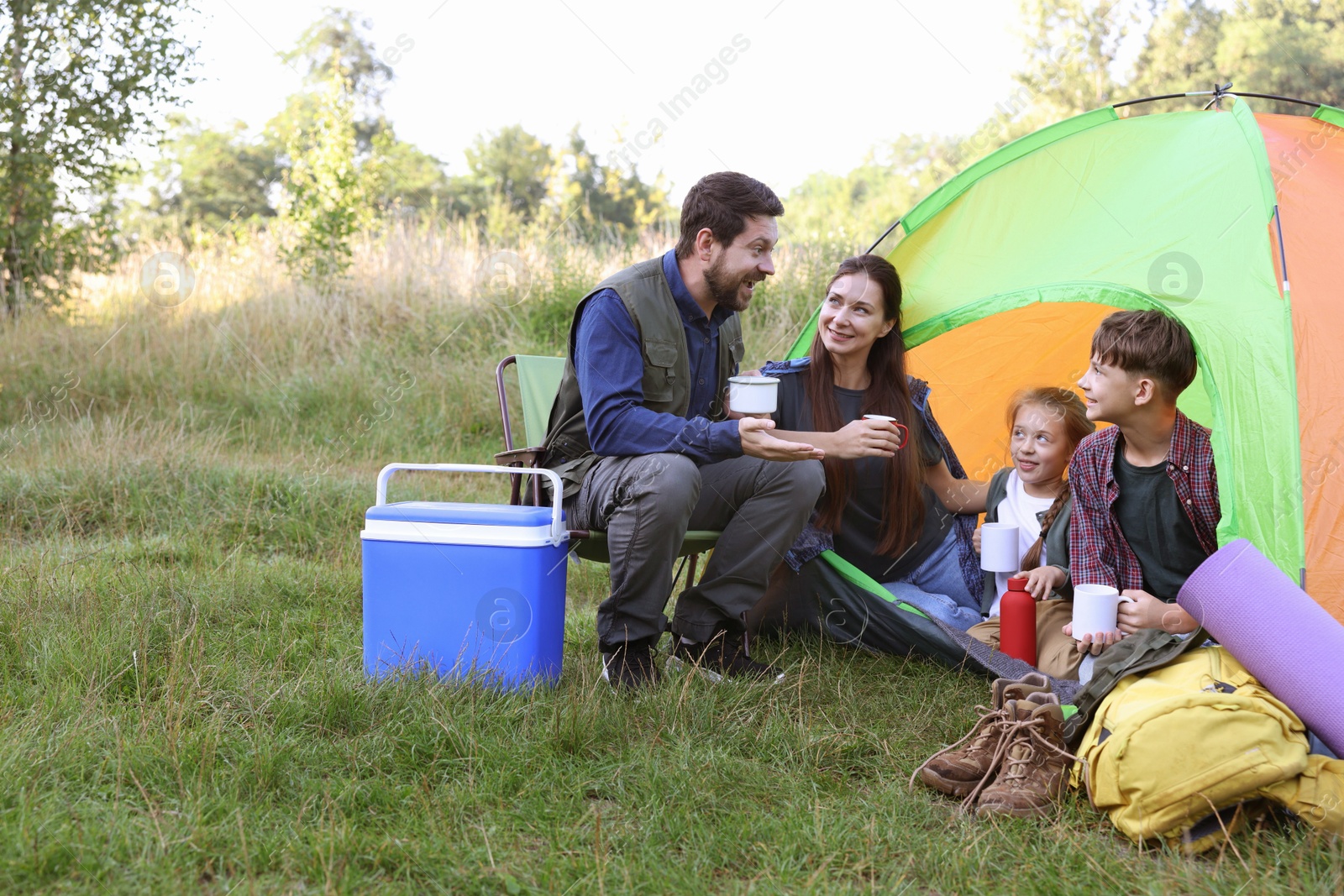 Happy family spending time together with camping tent, tourist equipment and mugs of hot drink outdoors Photo of Happy family spending time together with camping tent, tourist equipment and mugs of hot drink outdoors