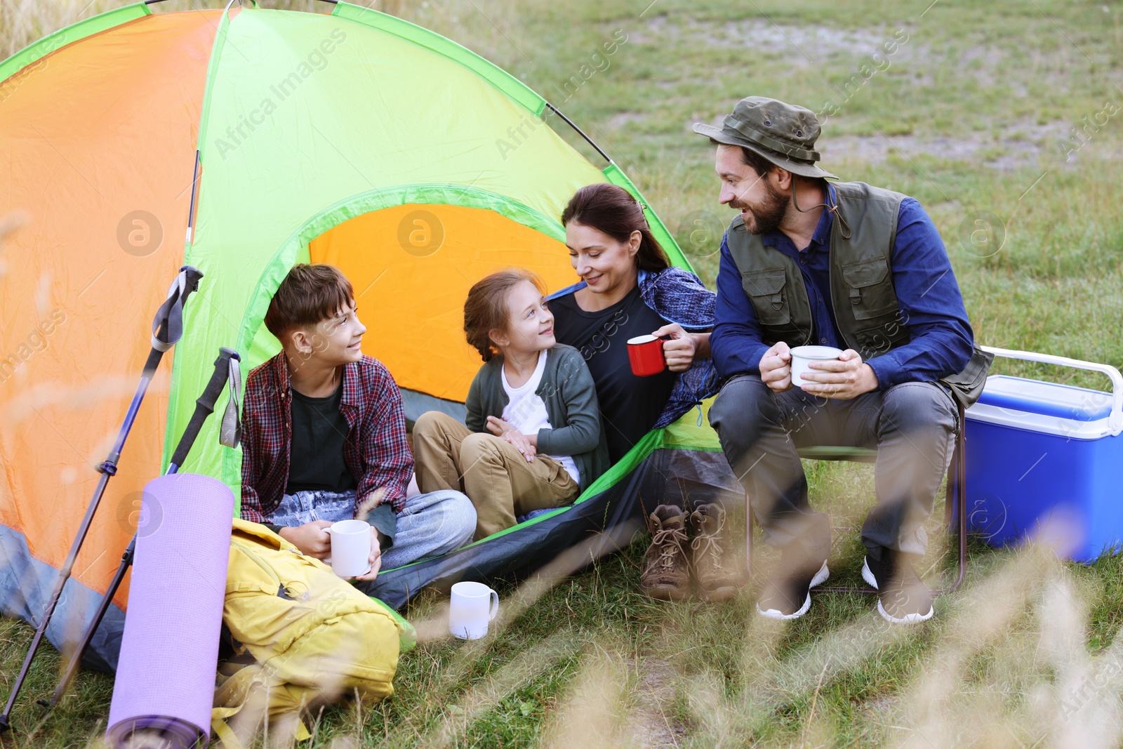 Photo of Happy family spending time together with camping tent, tourist equipment and mugs of hot drink outdoors