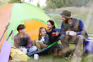 Photo of Happy family spending time together with camping tent, tourist equipment and mugs of hot drink outdoors