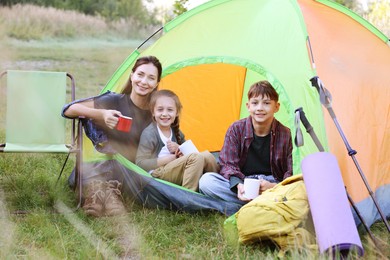 Photo of Happy family spending time together with camping tent, tourist equipment and mugs of hot drink outdoors
