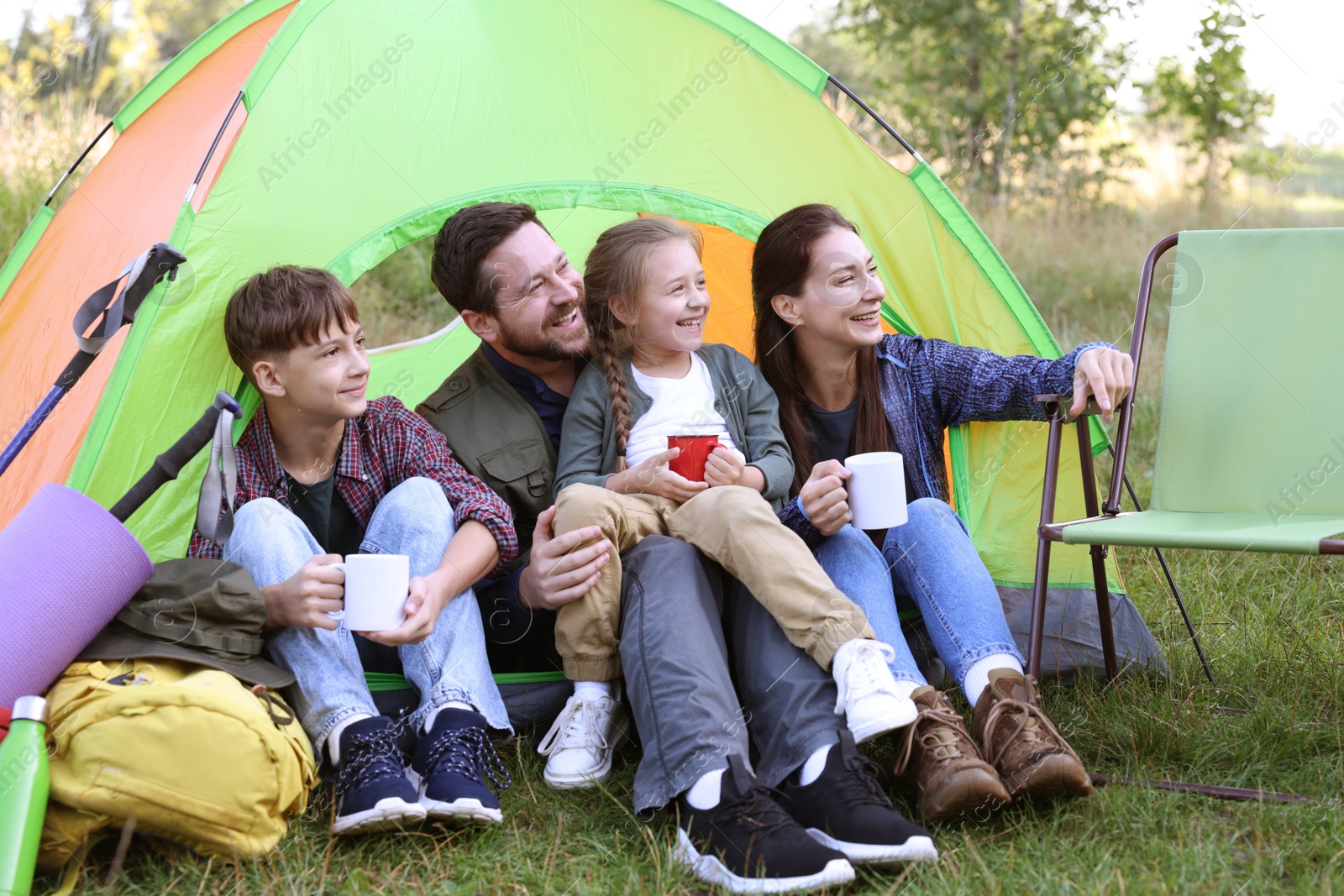 Photo of Happy family spending time together with camping tent, tourist equipment and mugs of hot drink outdoors