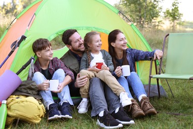 Photo of Happy family spending time together with camping tent, tourist equipment and mugs of hot drink outdoors
