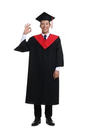 Photo of Young man in graduation gown and mortarboard showing OK gesture on white background