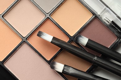 Photo of Beautiful eyeshadow palette and brushes on table, top view