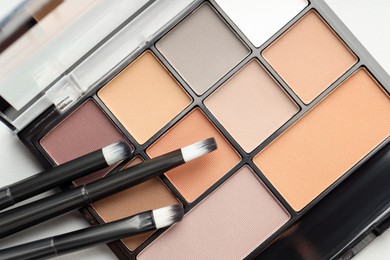 Photo of Beautiful eyeshadow palette and brushes on white table, top view