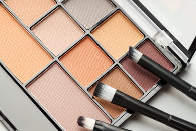 Photo of Beautiful eyeshadow palette and brushes on white table, top view