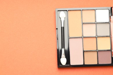 Photo of Beautiful eyeshadow palette and brush on pale orange background, top view. Space for text