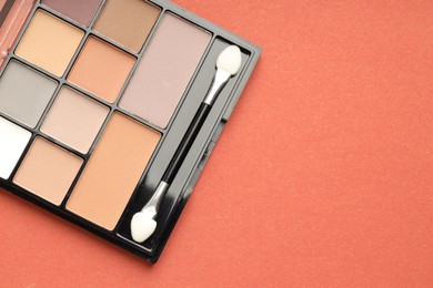 Photo of Beautiful eyeshadow palette and brush on coral background, top view. Space for text