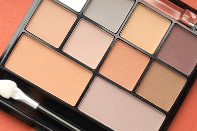Photo of Beautiful eyeshadow palette and brush on coral background, top view