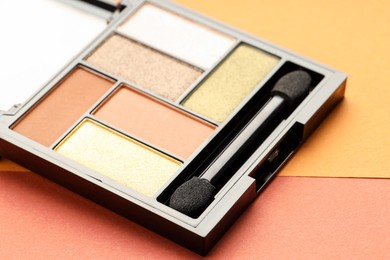Photo of Beautiful eyeshadow palette and brush on color background, closeup