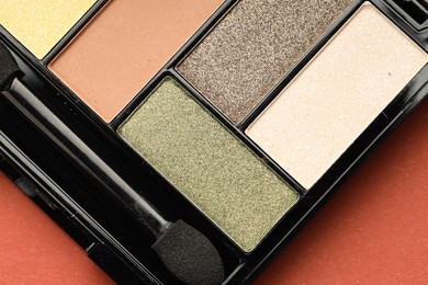 Photo of Beautiful eyeshadow palette and brush on coral background, top view