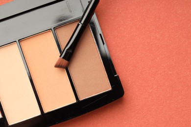 Photo of Beautiful eyeshadow palette and brush on coral background, top view. Space for text
