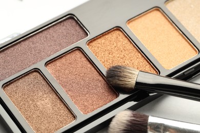 Photo of Beautiful eyeshadow palette and brushes on white background, closeup