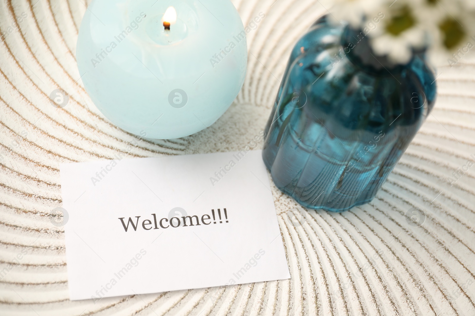 Card with word Welcome, burning candle and vase with flowers on white table, closeup Photo of Card with word Welcome, burning candle and vase with flowers on white table, closeup