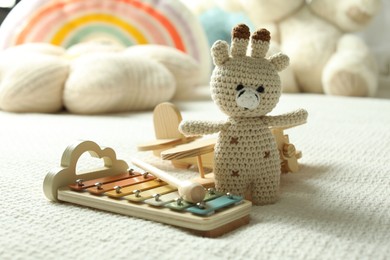 Photo of Cute giraffe, airplane and xylophone toys on bed, closeup