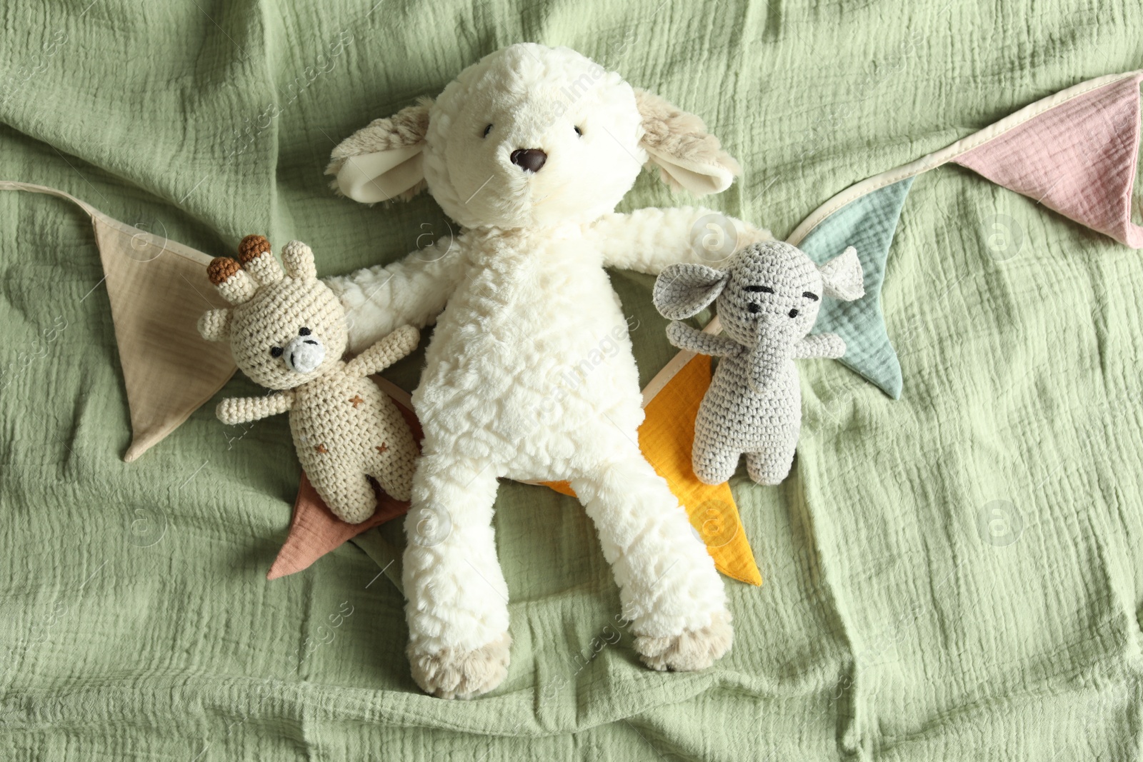 Photo of Cute soft toys and garland on olive fabric, top view