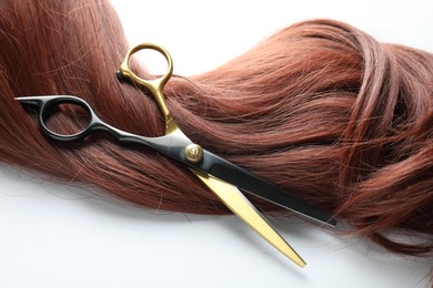 Photo of Auburn hair strand and hairdresser's scissors on white background, closeup