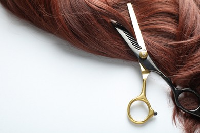 Photo of Auburn hair strand and hairdresser's scissors on white background, top view. Space for text