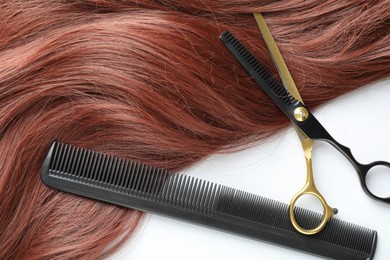 Photo of Auburn hair strand and hairdresser's tools on white background, flat lay