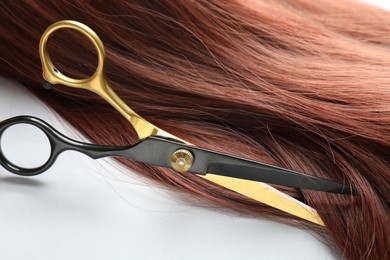 Photo of Auburn hair strand and hairdresser's scissors on white background, closeup