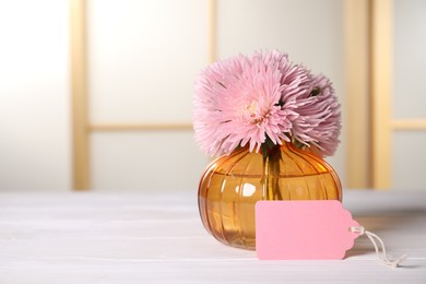 Photo of Blank card and flowers on white wooden desk indoors. Space for text