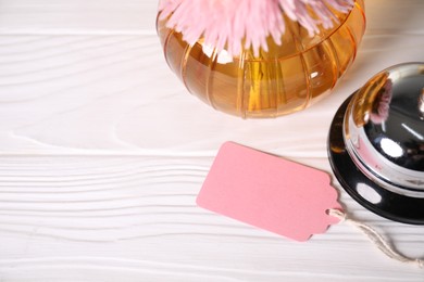 Photo of Blank card, desk bell and flowers on white wooden desk, closeup. Space for text