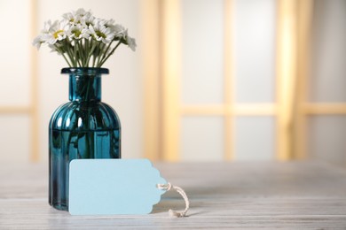 Photo of Blank card and flowers on white wooden desk indoors. Space for text