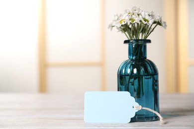 Photo of Blank card and flowers on white wooden desk indoors. Space for text