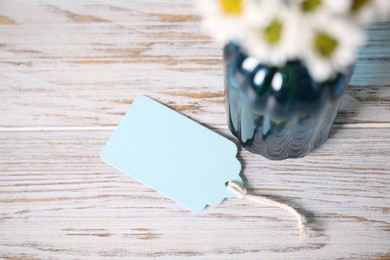 Photo of Blank card and flowers on white wooden desk, closeup. Space for text