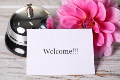 Photo of Card with word Welcome, desk bell and flower on white table, closeup