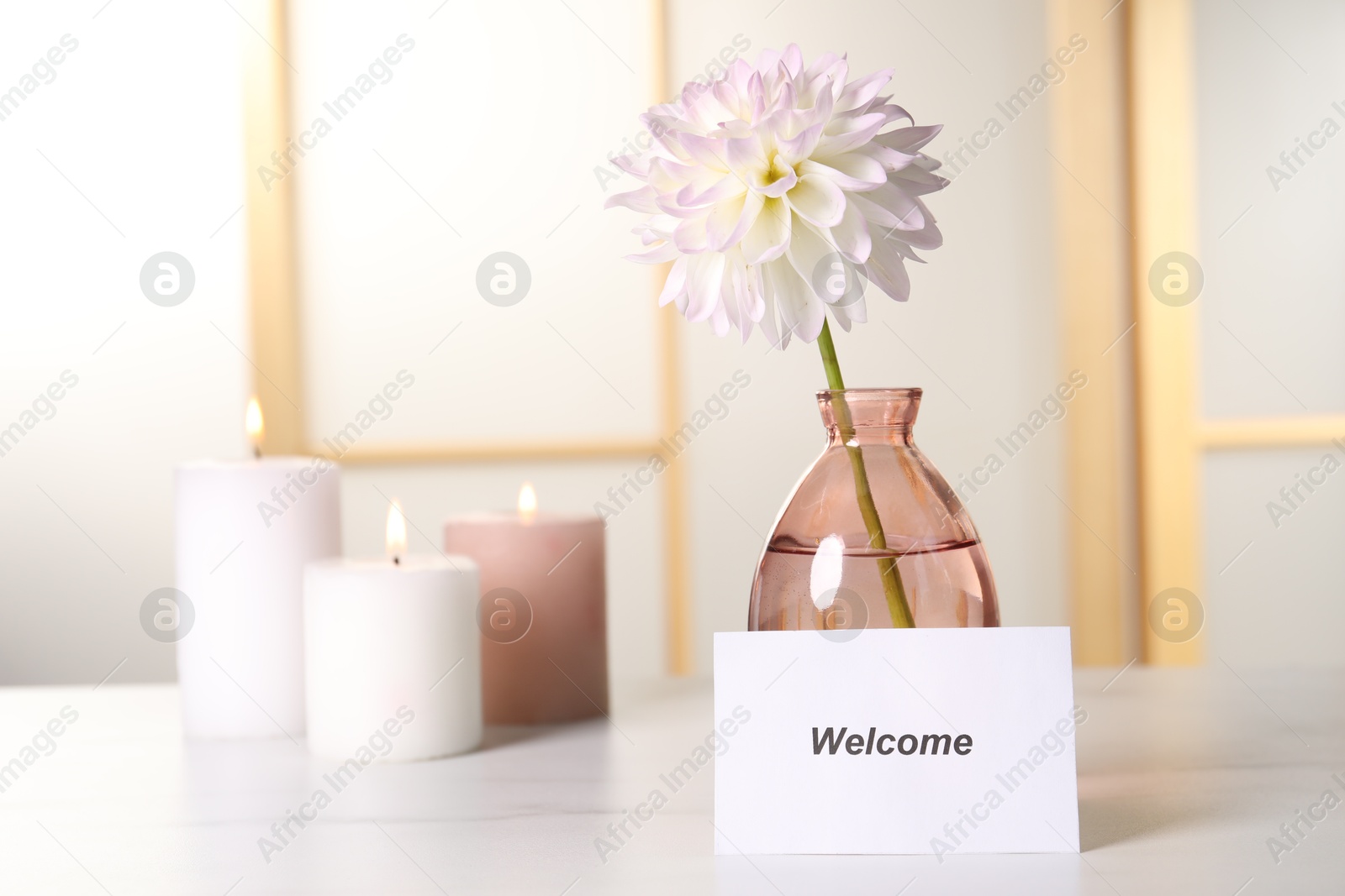 Card with word Welcome, vase with flower and burning candles on white table Photo of Card with word Welcome, vase with flower and burning candles on white table