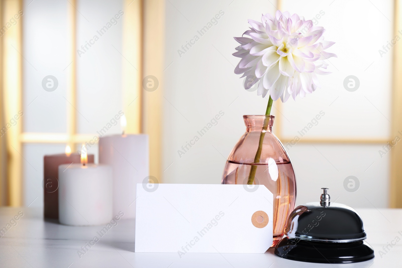 Photo of Blank card, desk bell, vase with flower and burning candles on white table indoors. Space for text