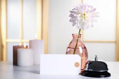 Photo of Blank card, desk bell, vase with flower and burning candles on white table indoors. Space for text