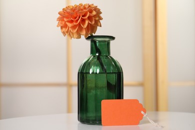 Photo of Blank card and flower on white table indoors. Space for text