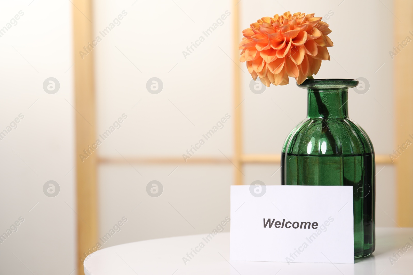 Card with word Welcome and vase with flower on white table indoors. Space for text Photo of Card with word Welcome and vase with flower on white table indoors. Space for text