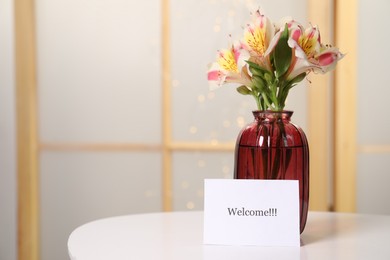 Photo of Card with word Welcome and vase with flowers on white table indoors. Space for text