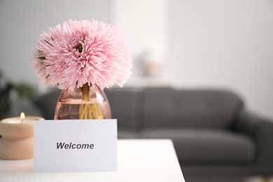 Photo of Card with word Welcome, vase with flowers and burning candle on white table indoors. Space for text