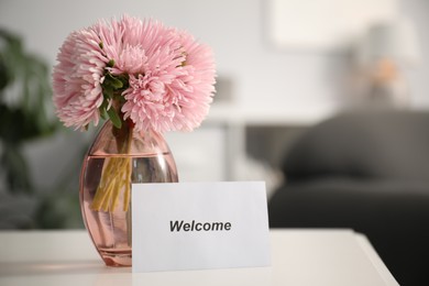 Photo of Card with word Welcome and vase with flowers on white table indoors. Space for text