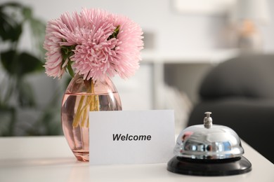 Photo of Card with word Welcome, vase with flowers and desk bell on white table indoors. Space for text