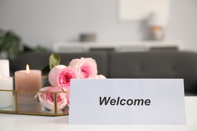 Photo of Card with word Welcome, roses and burning candles on white table. Space for text