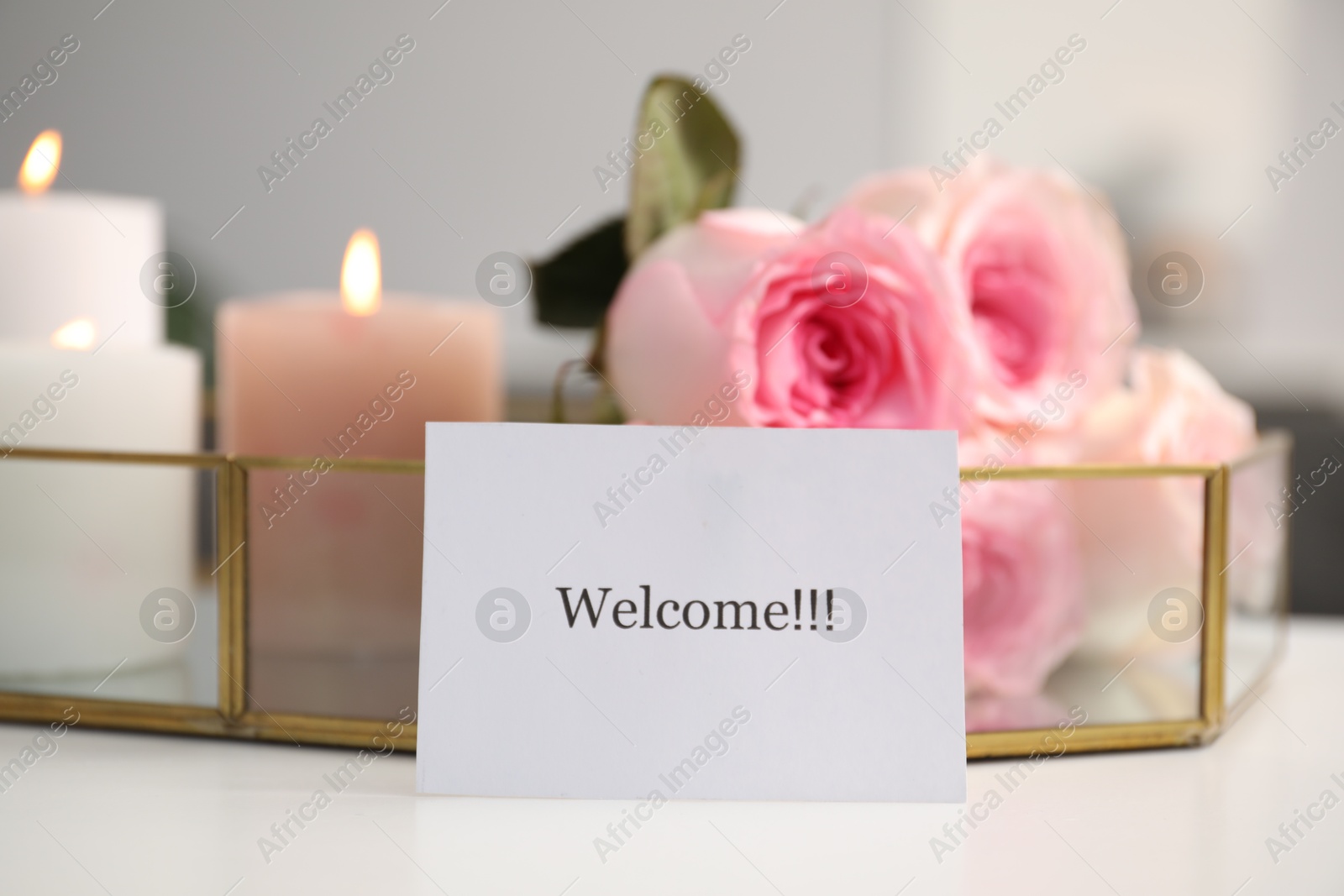 Card with word Welcome, roses and burning candles on white table, closeup Photo of Card with word Welcome, roses and burning candles on white table, closeup