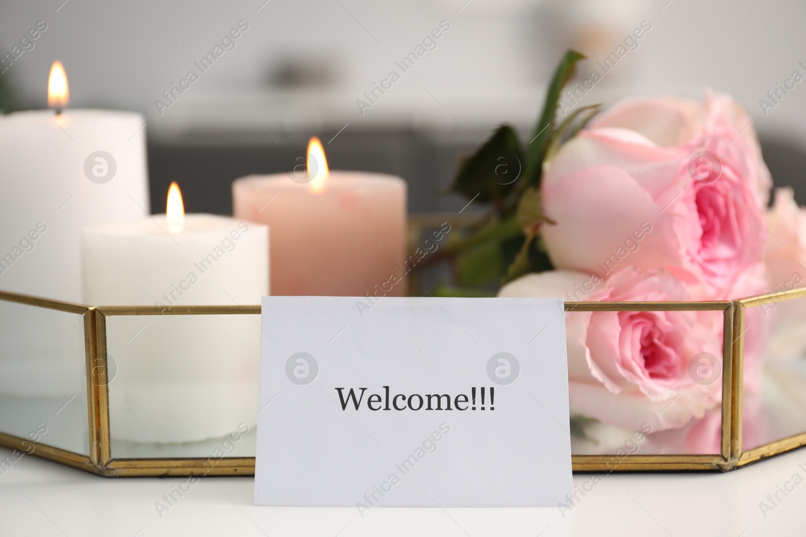 Card with word Welcome, roses and burning candles on white table, closeup Photo of Card with word Welcome, roses and burning candles on white table, closeup
