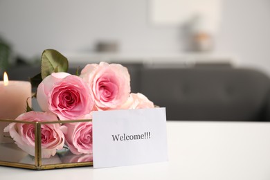Photo of Card with word Welcome, roses and burning candle on white table, closeup. Space for text
