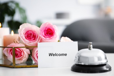 Photo of Card with word Welcome, desk bell and roses on white table, closeup