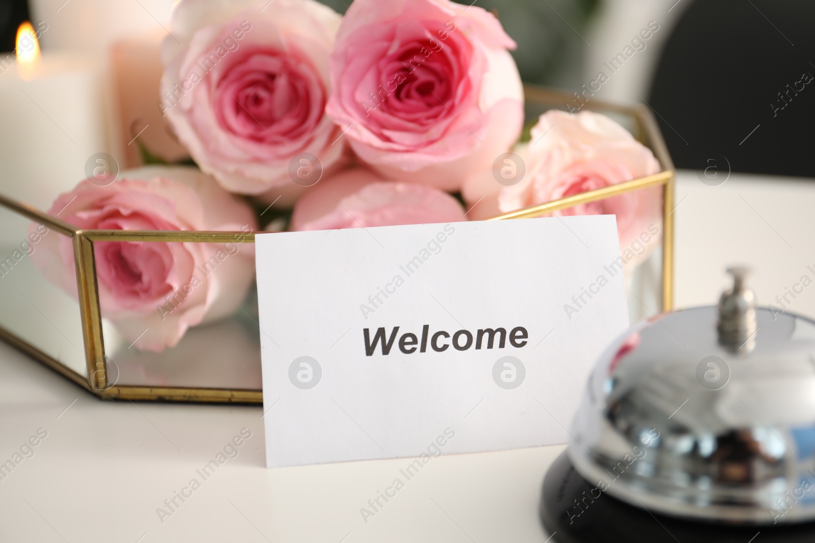 Photo of Card with word Welcome, desk bell and roses on white table, closeup
