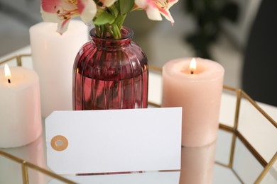 Photo of Blank card, vase with flower and burning candles on table indoors, closeup