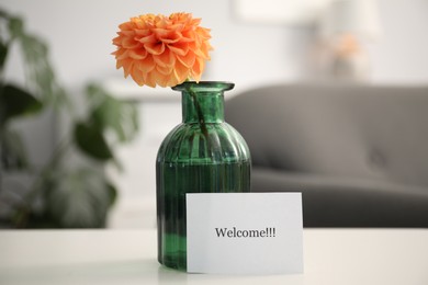 Photo of Card with word Welcome and vase with flower on white table indoors