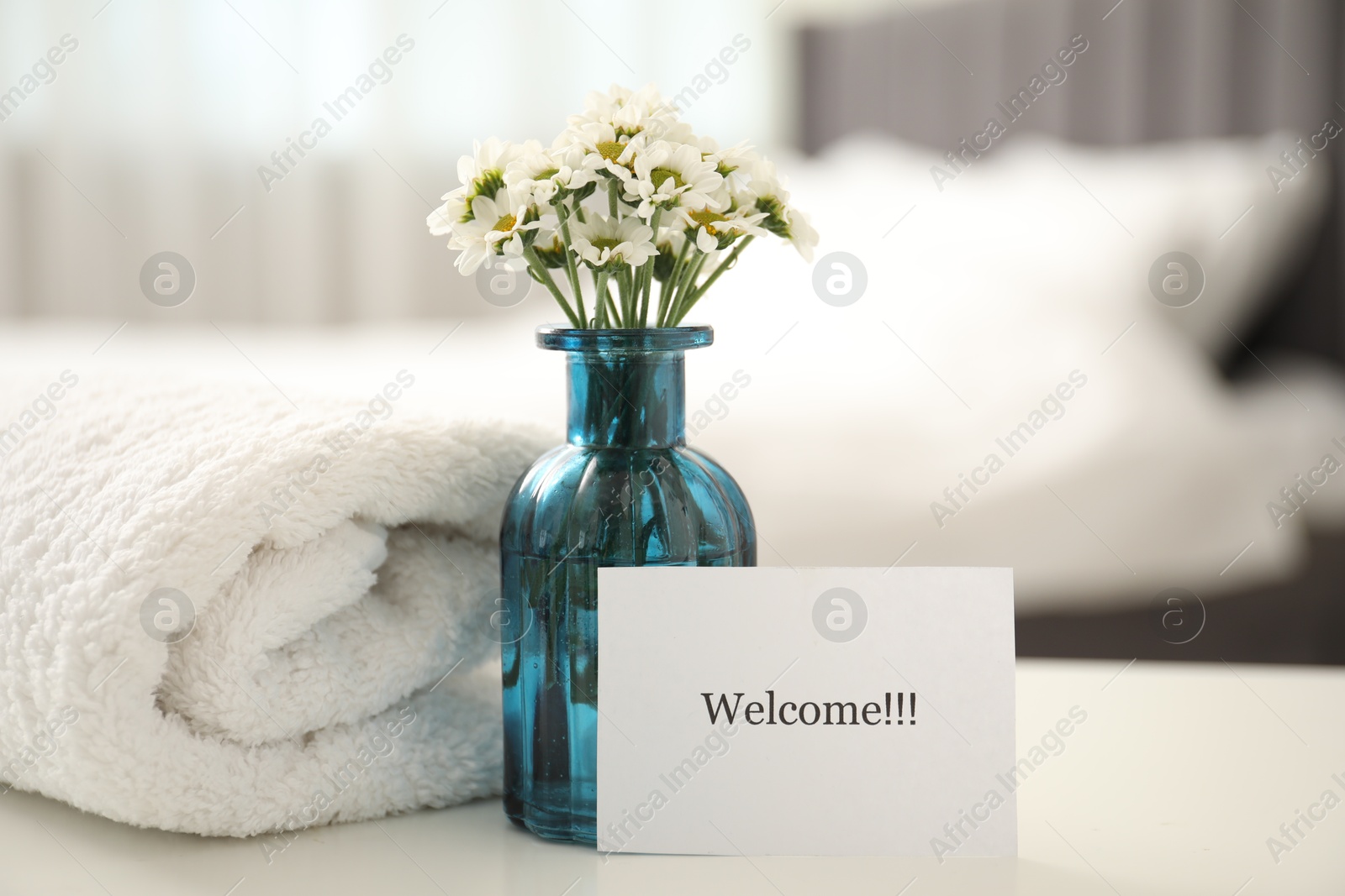 Photo of Card with word Welcome, vase with flowers and towel on white table indoors
