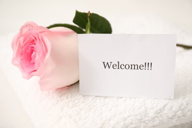 Photo of Card with word Welcome, rose and towel on white table, closeup
